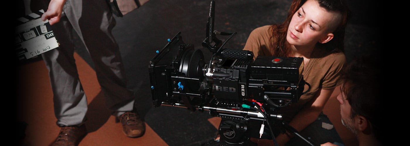 Two people are operating a large camera. A person is standing in front of them holding a clapper board. 