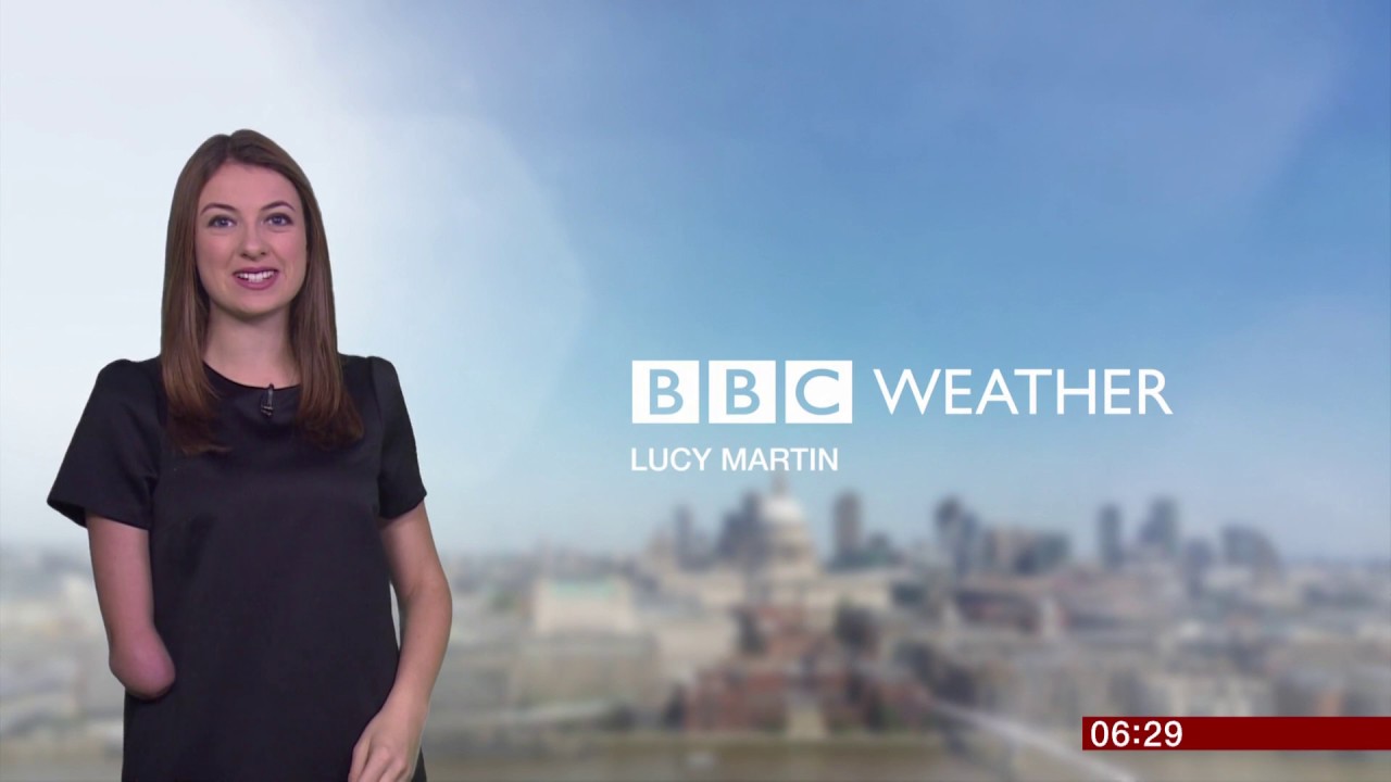 A person with long brown hair and limb difference on their right arm stands to the left of the image, facing the camera. The words "BBC weather" and "Lucy Martin" are displayed to the right of the screen. The background is cloudy. 