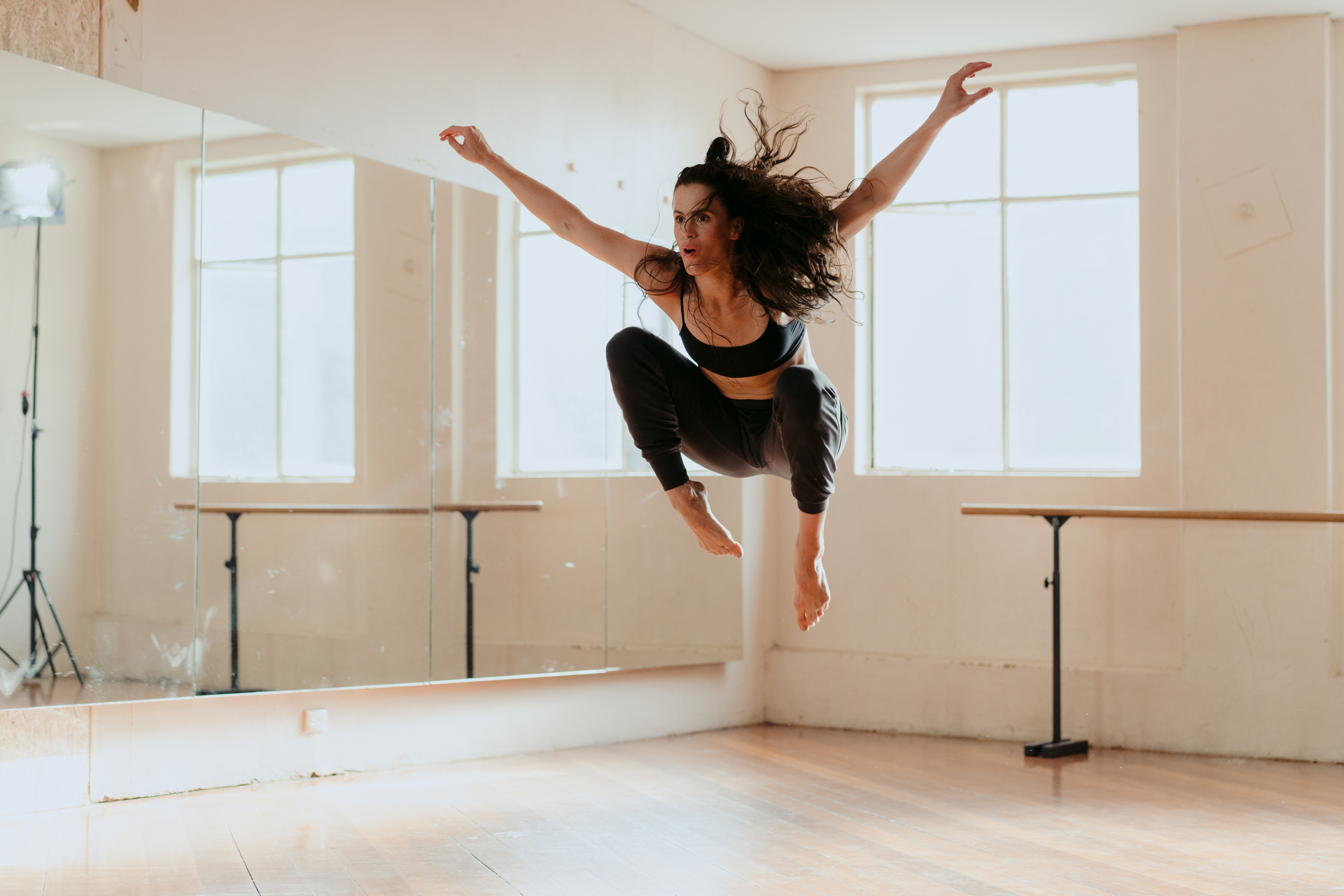 A female in a bright dance studio jumping energetically in the air